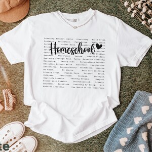 May include: White t-shirt with a black graphic that says "Homeschool" and lists a variety of homeschooling benefits, including "Learning Without Limits", "Family Time", "Real-Life Lessons", "Natural Learning", and "The World is Our Classroom".