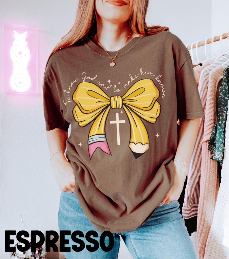 May include: A brown t-shirt with a yellow bow and a pencil with a cross on it. The text on the shirt reads "To know God and to make him known."