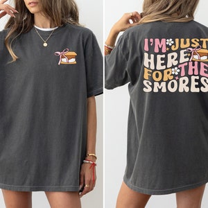 Op de afbeelding: Een donkergrijs oversized t-shirt met een afbeelding van een s'more op de voorkant en de tekst "I'm just here for the smores" op de achterkant.