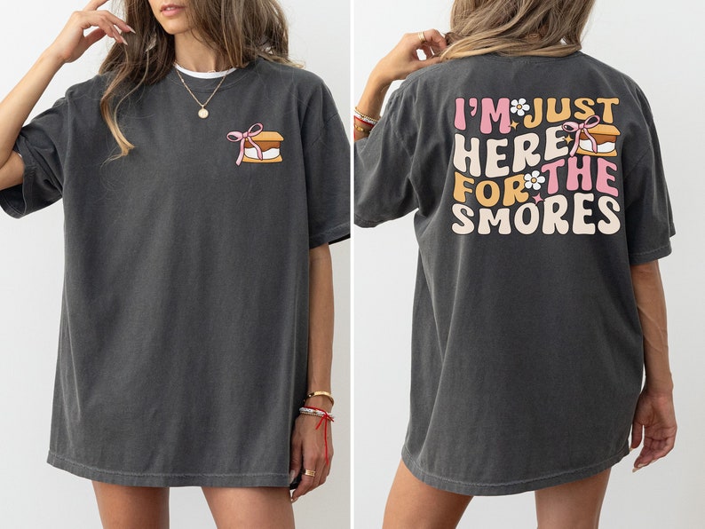 Op de afbeelding: Een donkergrijs oversized t-shirt met een afbeelding van een s'more op de voorkant en de tekst "I'm just here for the smores" op de achterkant.