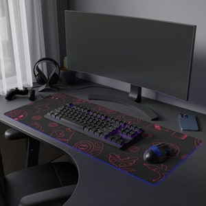 May include: A black gaming keyboard with a red and white design is on a black and red gaming mousepad with a blue LED light. A black computer monitor is in the background.