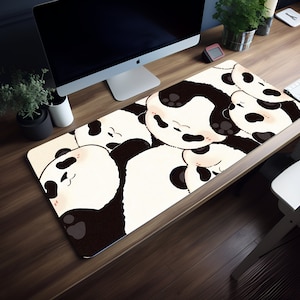 May include: A rectangular mouse mat with a repeating pattern of cartoon panda faces in black and white. The pandas have closed eyes and pink cheeks, creating a cute design. The mat is on a wooden desk.