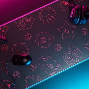 May include: A black gaming mouse and controller are on a black gaming mousepad with a pink and blue neon glow. The mousepad has a pattern of video game characters and objects in pink.