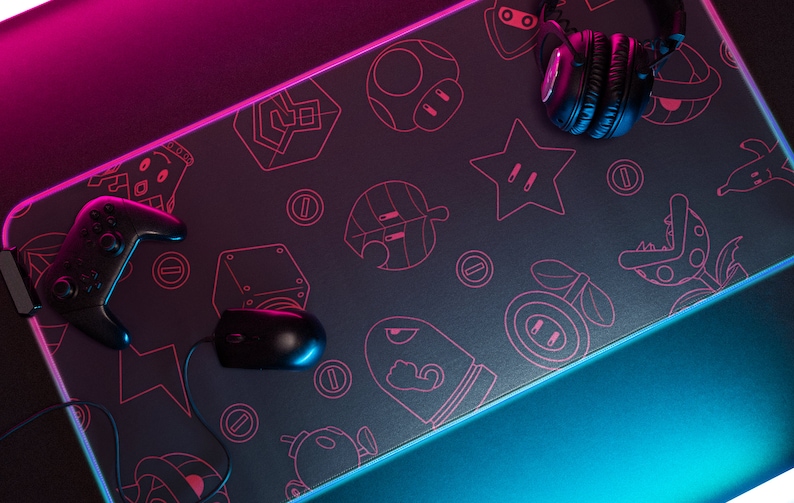 May include: A black gaming mouse and controller are on a black gaming mousepad with a pink and blue neon glow. The mousepad has a pattern of video game characters and objects in pink.