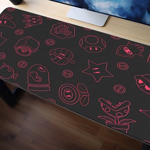 Könnte beinhalten: Eine schwarze Gaming-Mausmatte mit einem rosa Umriss verschiedener Videospielfiguren und -objekte. Die Figuren umfassen einen Stern, einen Pilz, eine Schildkröte, eine Pflanze und eine Bombe. Der Text "SNAPE" ist in der oberen rechten Ecke der Mausmatte sichtbar.