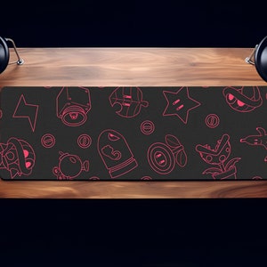 May include: A black gaming mouse pad with pink outlines of various video game characters and objects. The characters include a star, a mushroom, a plant, a shell, and a creature with a mouth.