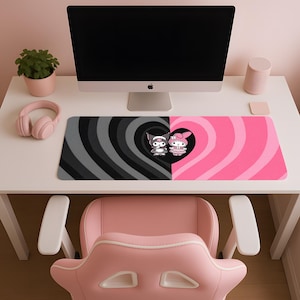 May include: A pink and black mousepad featuring a cartoon heart design with two characters. The left side has a black and gray swirl pattern, while the right side is pink. The mousepad is on a white desk with a computer monitor, headphones, and a pink chair.