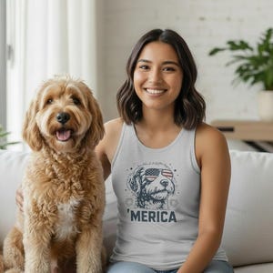 May include: A light grey vest top featuring a graphic illustration of a dog wearing American flag-patterned sunglasses, with the text 'MERICA printed in bold dark blue capital letters underneath the dog's face, centred on the chest.