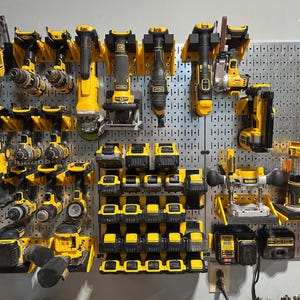 May include: A selection of yellow and black power tools, such as drills and saws, mounted on a grey pegboard. The image also shows various battery packs, demonstrating a comprehensive tool organisation system.