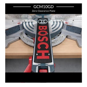 Puede incluir: Una placa de compensación Bosch GCM10GD para una sierra ingletadora. La placa es negra con letras rojas y un asa roja. La sierra tiene un protector de hoja plateado y una base de madera.