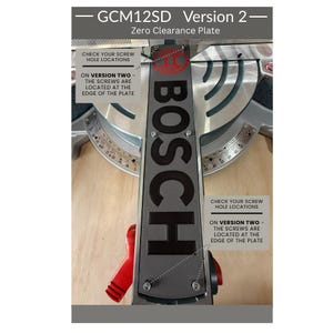 May include: A grey Bosch GCM12SD Version 2 zero clearance plate for a mitre saw. The plate features black text reading BOSCH, with labels indicating that screw holes are located at the edge of the plate for this specific version of the component.