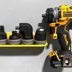 Könnte beinhalten: Ein gelber und schwarzer DeWalt 12V Brushless Bohrer mit einem angeschlossenen Akku, der an einer gelben Wandhalterung hängt. Die Halterung hält vier schwarze Bohrer.