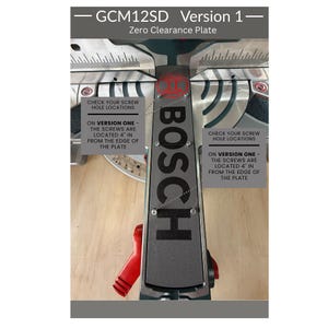 May include: A grey Bosch GCM12SD Version 1 zero clearance plate for a mitre saw. The plate features the Bosch logo and text indicating that screws are located 10.16 cm in from the edge of the plate. The component is metallic with visible screw holes.