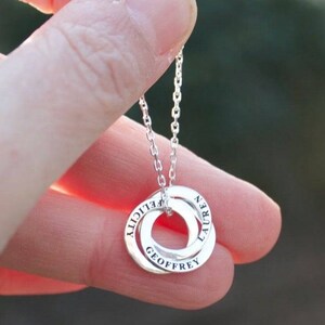 May include: Silver necklace with a double ring pendant. The rings are engraved with the names "Geoffrey", "Lily", and "Virgil".