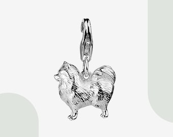 May include: A silver charm in the shape of a Pomeranian dog. The charm has a detailed design and is attached to a silver clasp.