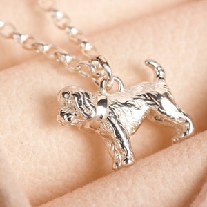 May include: A silver charm necklace with a detailed, three-dimensional dog pendant. The dog is standing on all four paws with its head tilted slightly to the side. The chain is a delicate, silver curb chain.