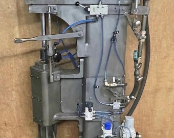 May include: A gray industrial machine with a large metal cylinder and a series of pipes and valves. The machine is mounted on a wooden surface and has a label that reads "IMG_2939".