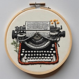 Puede incluir: Bordado de una máquina de escribir vintage con un diseño en blanco y negro. La máquina de escribir tiene una cinta roja y naranja y un diseño de flores amarillas en el lateral. La obra de arte está enmarcada en un aro de madera.
