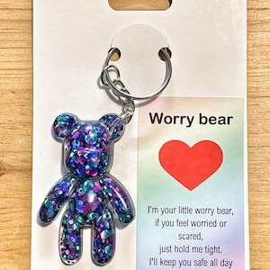 May include: A resin bear keyring filled with purple, blue, and teal glitter attached to a white display card. The card features a red heart and the text: Worry bear, I'm your little worry bear, if you feel worried or scared, just hold me tight.