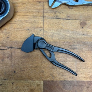 Może przedstawiać: Czarny klucz regulowany z srebrnym logo KNIPEX. Klucz leży na drewnianej powierzchni.