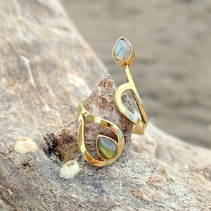 May include: A gold ring featuring two teardrop-shaped labradorite gemstones. The ring is crafted with a swirling, organic design.