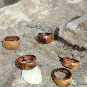 Può includere: Sei anelli di legno marroni con un motivo a venature di legno naturale. Gli anelli sono disposti su un pezzo di legno di deriva.