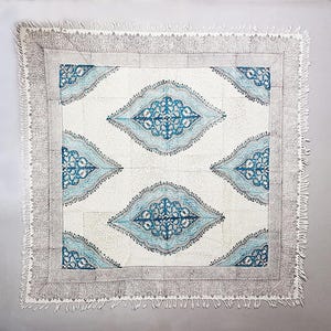 May include: A white cotton throw blanket with a blue and white geometric pattern. The blanket has a fringe border.