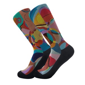 May include: Two colorful socks with abstract patterns. The socks feature a mix of colors, including blue, red, yellow, and brown, with black heels and toes. The design is a blend of geometric shapes and organic forms.