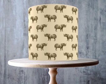 May include: A beige cake drum with a white cake decorated with a repeating pattern of brown rhinoceroses. The cake is on a wooden cake stand. The cake is labelled as vegan, gluten-free, dairy-free, nut-free, and GMO-free.