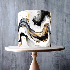 May include: A white cake with black and gold marbling on a wooden cake stand. The cake is decorated with a black and gold abstract design. The cake is nut-free, dairy-free, gluten-free, vegan, and GMO-free.