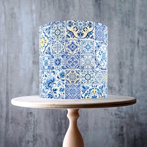 Peut inclure: Un gâteau orné d'un motif de carreaux bleus et blancs, présenté sur un présentoir à gâteau en bois clair. Le présentoir a un dessus rond et une base en piédestal. L'image comprend le texte "MADE IN THE UK" et un symbole indiquant que le produit est végétalien, sans gluten et sans OGM.