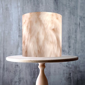 May include: A light-colored cake stand with a cylindrical cake covered in a fluffy, peach-colored fur-like design. The stand is made of light-colored wood and has a round top and base. The cake stand is approximately 10 inches in diameter.