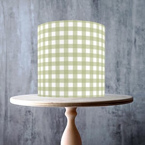 May include: A light green and white checkered cake wrap sits on a wooden cake stand. The stand has a round top and a pedestal base. The background is a gray wall. The cake wrap is cylindrical.