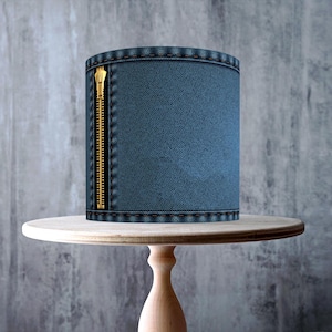 May include: A cake decorated to resemble denim, featuring a gold zipper detail. It is presented on a light wooden cake stand. The image includes a "Made in the UK" sticker and a "GMO Free, Vegan, Gluten Free, Dairy Free, Nut Free" sticker.