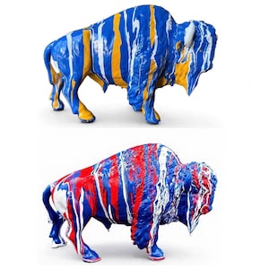 May include: Two standing bison sculptures featuring a glossy finish with vertical paint drip patterns. The top bison displays blue, yellow, and white colors, while the bottom bison features red, blue, and white paint drips across its body.