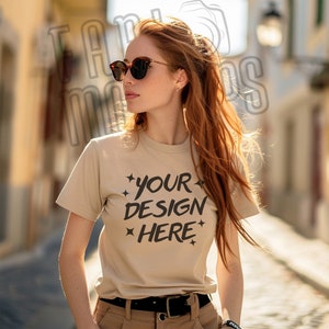 May include: A woman wearing a beige t-shirt with the text "YOUR DESIGN HERE" printed on the front. She is wearing sunglasses and has long, red hair.