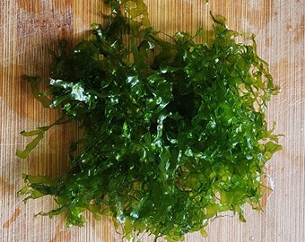 May include: A pile of fresh, dark green seaweed on a wooden cutting board.