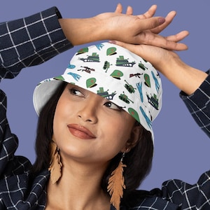 May include: A white bucket hat with a pattern of military-themed illustrations, including tanks, airplanes, and soldiers. The hat has a blue and green color scheme.