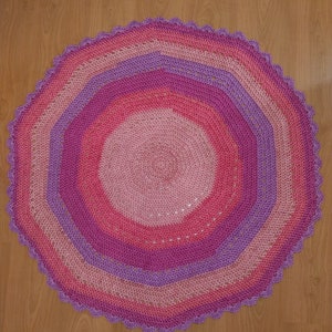 Peut inclure: Un tapis rond crocheté avec un bord festonné dans des tons de rose et de violet.
