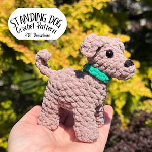 May include: A crocheted dog in a standing position, with a green collar and black eyes. The dog is a light brown color and has a textured appearance. The image includes text that reads "STANDING DOG Crochet Pattern PDF Download".