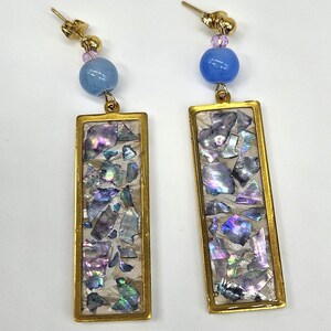 May include: A pair of gold-toned rectangular earrings. Each earring features a gold frame filled with iridescent, mosaic-like pieces. A light blue bead and a smaller pink bead are attached above each rectangle.