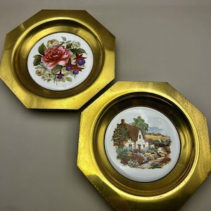 Puede incluir: Dos bandejas octogonales de latón vintage. Cada bandeja presenta un inserto de cerámica blanca con un diseño pintado. Una representa una rosa y un arreglo floral, la otra una escena de cabaña. Las bandejas tienen un acabado dorado.