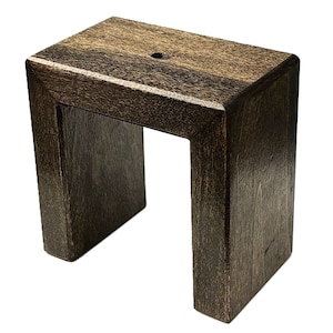 May include: A dark brown wooden stand with a square top and a rectangular opening in the center. The stand is made of solid wood and has a smooth finish.