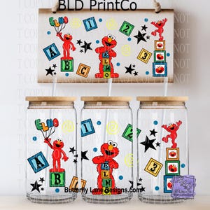 May include: Set of three clear glass tumblers with wooden lids, each featuring Elmo graphics and Sesame Street-themed designs. The set includes a wooden sign with Elmo and block graphics. The sign reads "BLD PrintCo".
