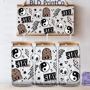 May include: Clear glass beverage cups with bamboo lids, decorated with black and white graphics including skulls, yin yang symbols, lightning bolts, and beanies. A wooden sign above repeats the design with the text "STAY".