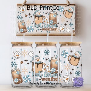 May include: Three clear glass tumblers with bamboo lids and straws, decorated with a winter-themed design. The design includes snowmen, hot cocoa, snowflakes, and the text "hot cocoa weather". A wooden sign with the text "BLD PrintCo" is above the tumblers.