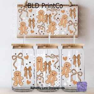 May include: Three glass tumblers with bamboo lids and straws, decorated with a gingerbread man, bows, and hearts. A matching sign hangs above with the text "BLD PrintCo". The design is repeated on the tumblers. The website "Butterfly Lane Designs.com" is visible.