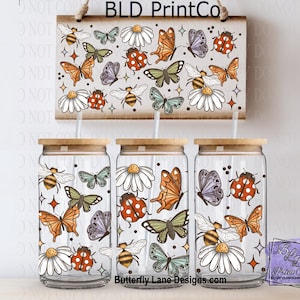 May include: Three glass tumblers with wooden lids and a matching wooden sign, all decorated with a repeating pattern of butterflies, bees, ladybugs, and daisies. The sign is suspended by a rope. The tumblers have a capacity of approximately 16 ounces.