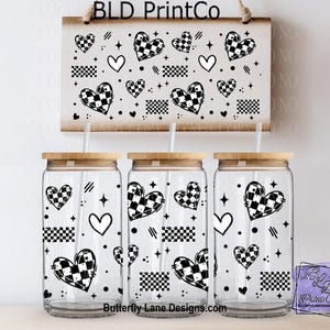 May include: Three clear glass tumblers with bamboo lids and straws, decorated with black and white checkered hearts, stars, and geometric shapes. A matching sign hangs above. The sign and tumblers have the text "BLD PrintCo" and "Butterfly Lane Designs".