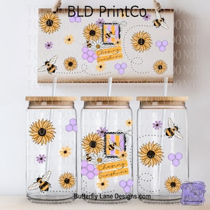May include: Three clear glass tumblers with bamboo lids, decorated with sunflowers, bees, and honeycomb patterns. The text "Chasing Sunshine" is featured on the center tumbler. A matching wooden sign hangs above.